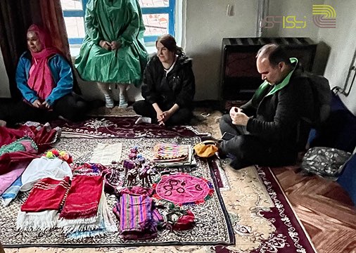 گروهی از همسفران در خانه‌ای روستایی در روستای قلعه قافه استان گلستان مشغول بازدید و خرید صنایع دستی ( منسوجات دستباف ) هستند